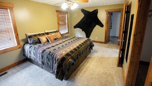 Un dormitorio con cama, ventilador de techo, un trozo de piel de animal en la pared y una puerta que da a otra habitación.