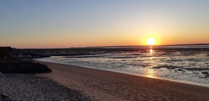Uma praia com um pôr do sol, águas calmas e um cais.