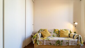 Una habitación con un sofá apoyado en la pared, una lámpara y suelo de madera.