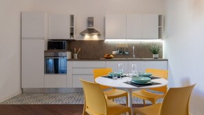 Una cocina moderna con armarios blancos, microondas y un comedor con sillas amarillas y una mesa blanca.