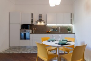 Eine moderne Küche mit weißen Schränken, einer Mikrowelle und einem Essbereich mit gelben Stühlen und einem weißen Tisch.