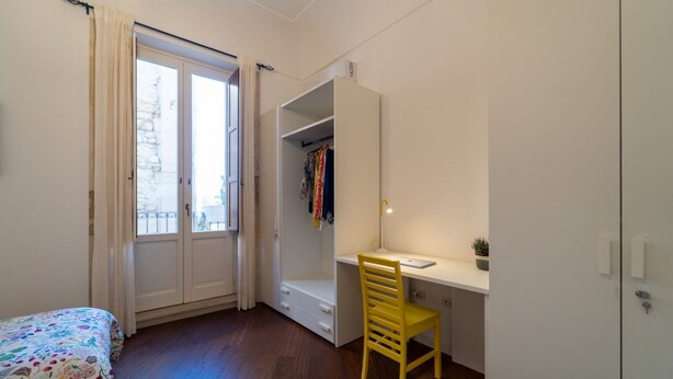 Un dormitorio con cama, escritorio, silla, armario y ventana.