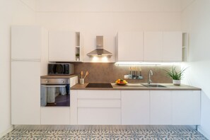 A modern kitchen with white cabinets, a microwave, an oven, a sink, and a countertop with a bowl of fruit. - GuestHost - Cozy and bright 87 square meters apartment, perfect for five people, located on the second floor of a building (no elevator).The property is located on the island of Ortigia (Restricted-Traffic Area), the historic and cultural heart of Syracu (Syracuse)