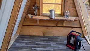 A wooden loft bedroom with a sloped ceiling, a window, a metal kettle, a glass jar, and a portable heater on the floor. - Tiny A frame cabin in the forest (Templeton)