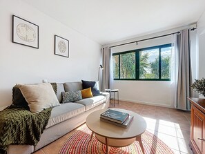Un salon moderne avec un canapé gris, une table basse ronde et une grande fenêtre avec des rideaux.