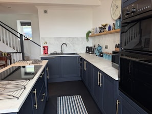 Une cuisine moderne avec des meubles de rangement bleu foncé, un plan de travail en marbre, une cuisinière noire et une horloge au mur.