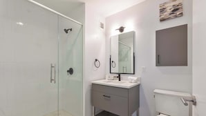 A modern bathroom with a glass shower enclosure, a vanity with a mirror, and a toilet. - Luxury Apt Near Kendall Square (Cambridge, MA)