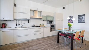 Een moderne keuken met witte kasten, roestvrijstalen apparatuur en een glazen eettafel met rieten stoelen.