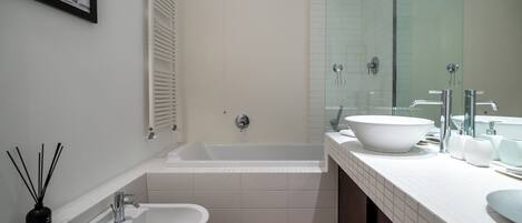 Ein modernes Badezimmer mit einer Badewanne, zwei Waschbecken, einem Bidet und einem großen Spiegel.