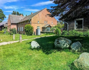 Un bâtiment en briques avec un toit en pente, un chemin pavé et de gros rochers au premier plan.