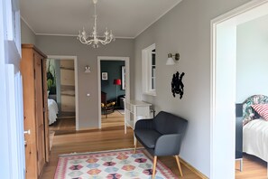 A spacious room with a chandelier, a sofa, a bed with a floral headboard, and a view into another room.