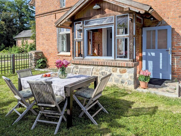 A rustic brick house with a stone foundation, a wooden porch, and a dining area with a table and chairs.