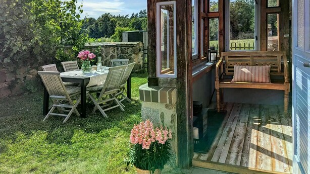 A patio with a table and chairs, a wooden bench, and a glass door leading to an outdoor area. - Holiday Home Sommergrün with Garden (Nordwestuckermark)