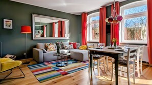 A modern living room with a sofa, dining table, and chairs, a large mirror, and a view of the outdoors. - Holiday Home Sommergrün with Garden (Nordwestuckermark)