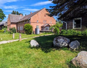 En murstensbygning med skråt tag, en belagt sti og store sten i forgrunden.