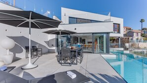 A modern outdoor pool area with a glass-enclosed dining space and lounge chairs. - Villa Alba VI4498 by Riviera Holiday Homes (Niza)