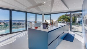 A modern kitchen with large windows, a central island, and a view of the city. - Villa Alba VI4498 by Riviera Holiday Homes (Niza)