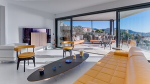 A modern living room with a large glass wall, a sofa, chairs, and a coffee table. - Villa Alba VI4498 by Riviera Holiday Homes (Niza)