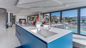 A modern kitchen with a large island, a sink, and a view of the city through large windows. - Villa Alba VI4498 by Riviera Holiday Homes (Niza)