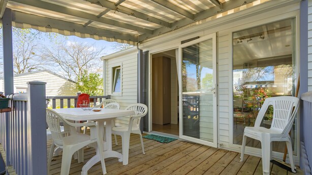 Varanda coberta com mesa, cadeiras, porta de correr de vidro e vista para o exterior.