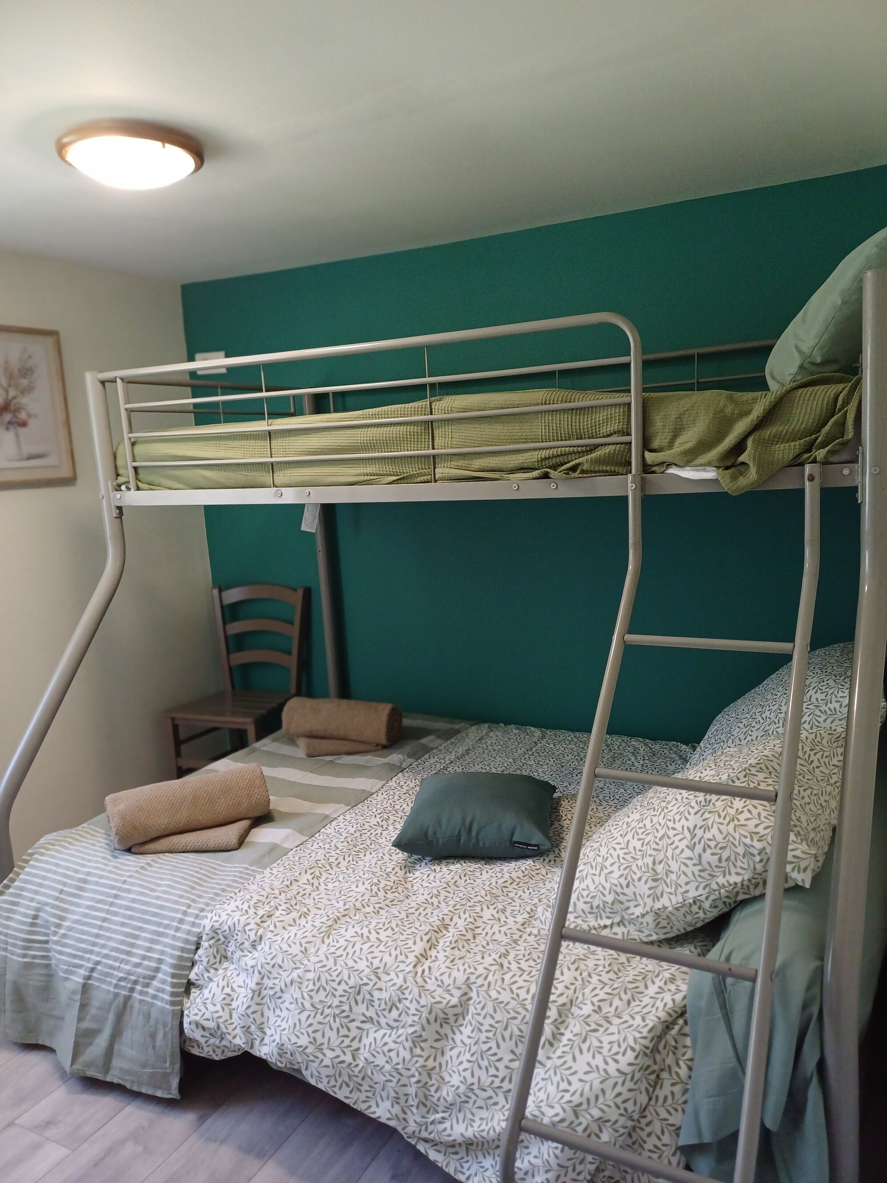 A bunk bed with a green mattress, a patterned pillow, and a rolled towel on the lower bunk.