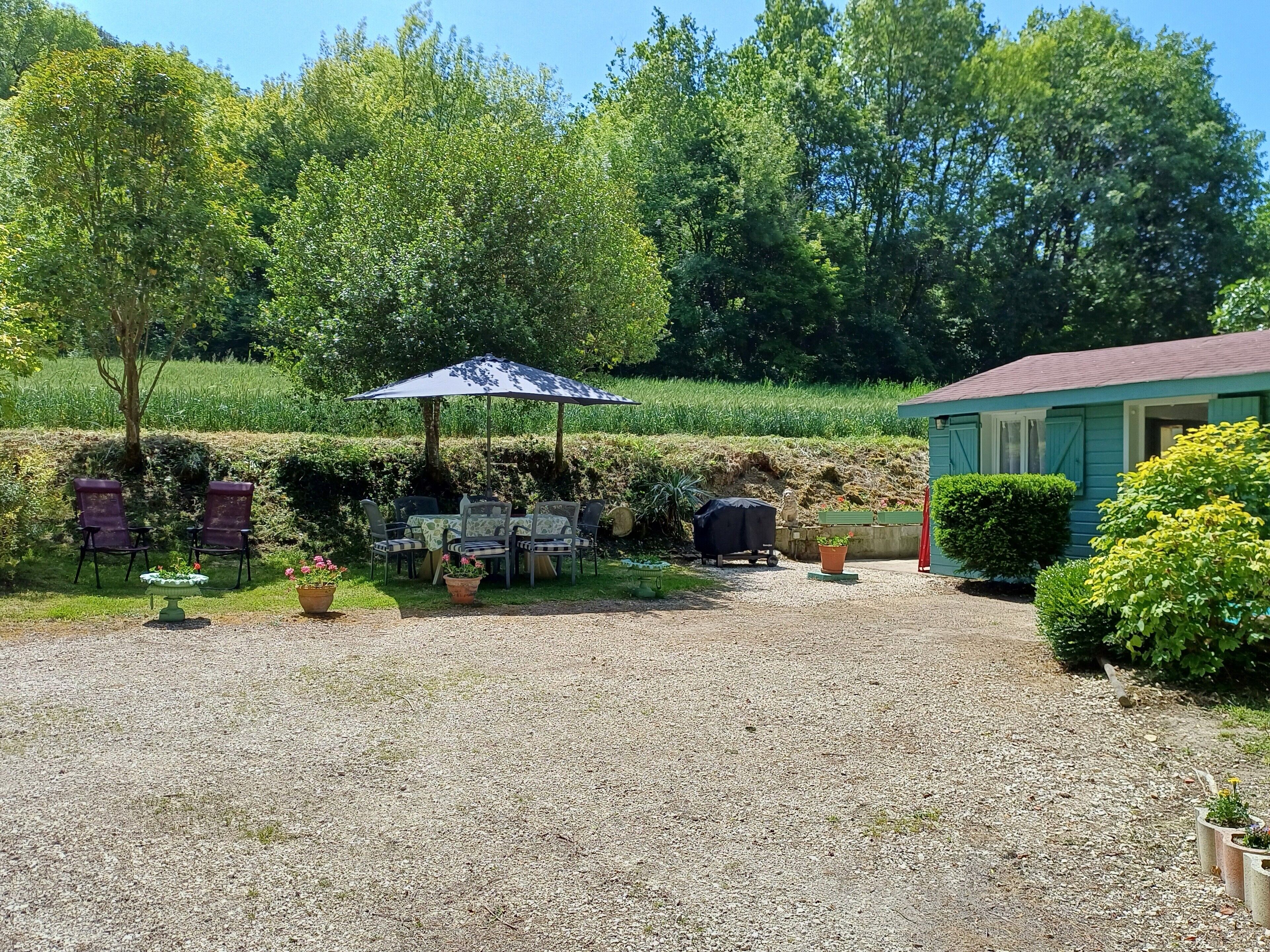 A gravel patio with outdoor seating, a covered table, and a small building.