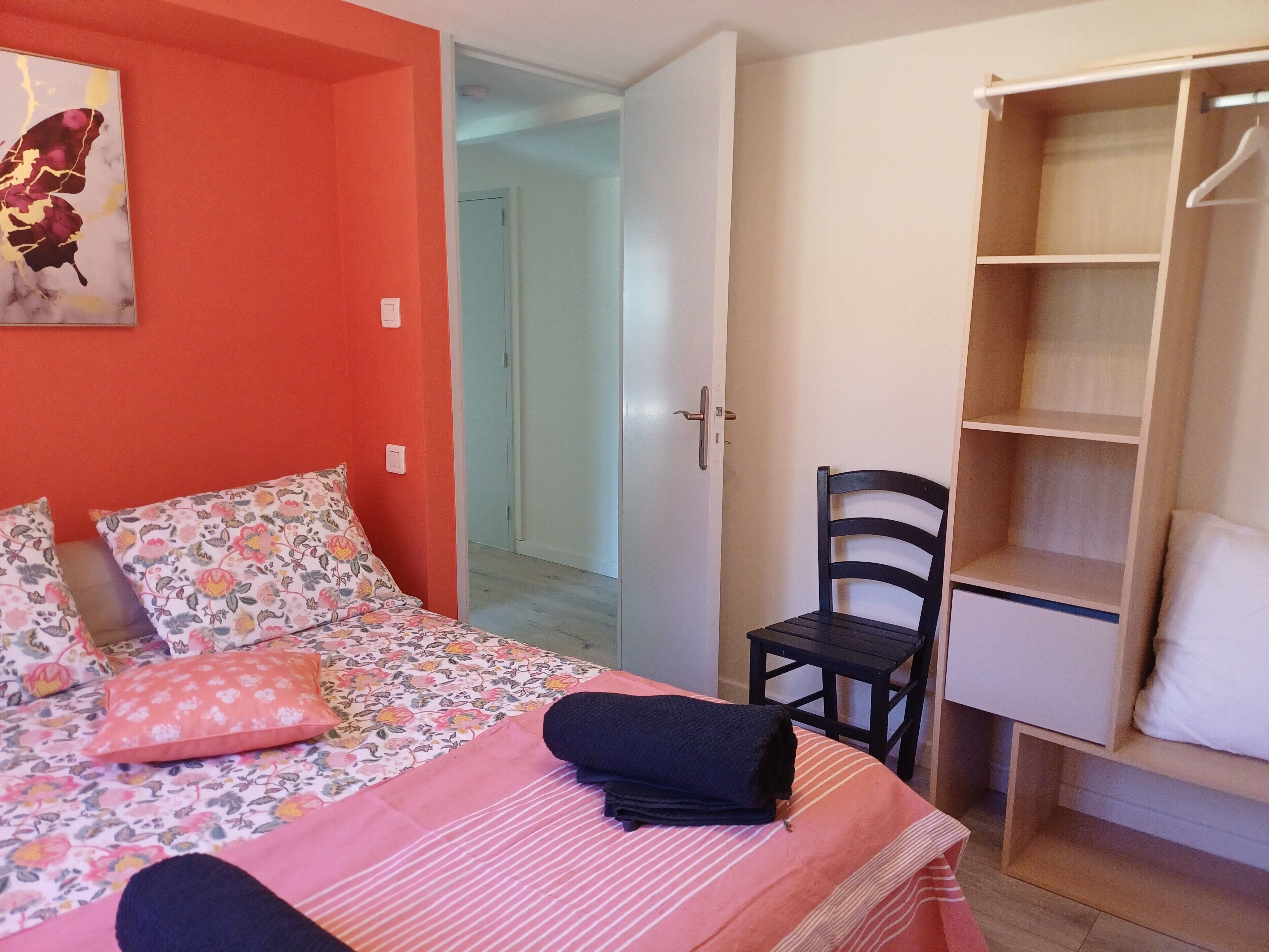A bedroom with a bed, a chair, a wardrobe, and a door leading to another room.