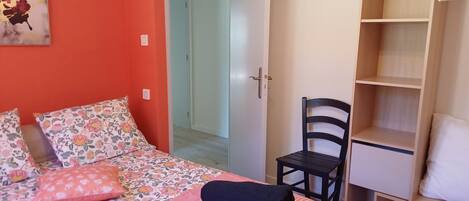 A bedroom with a bed, a chair, a wardrobe, and a door leading to another room.