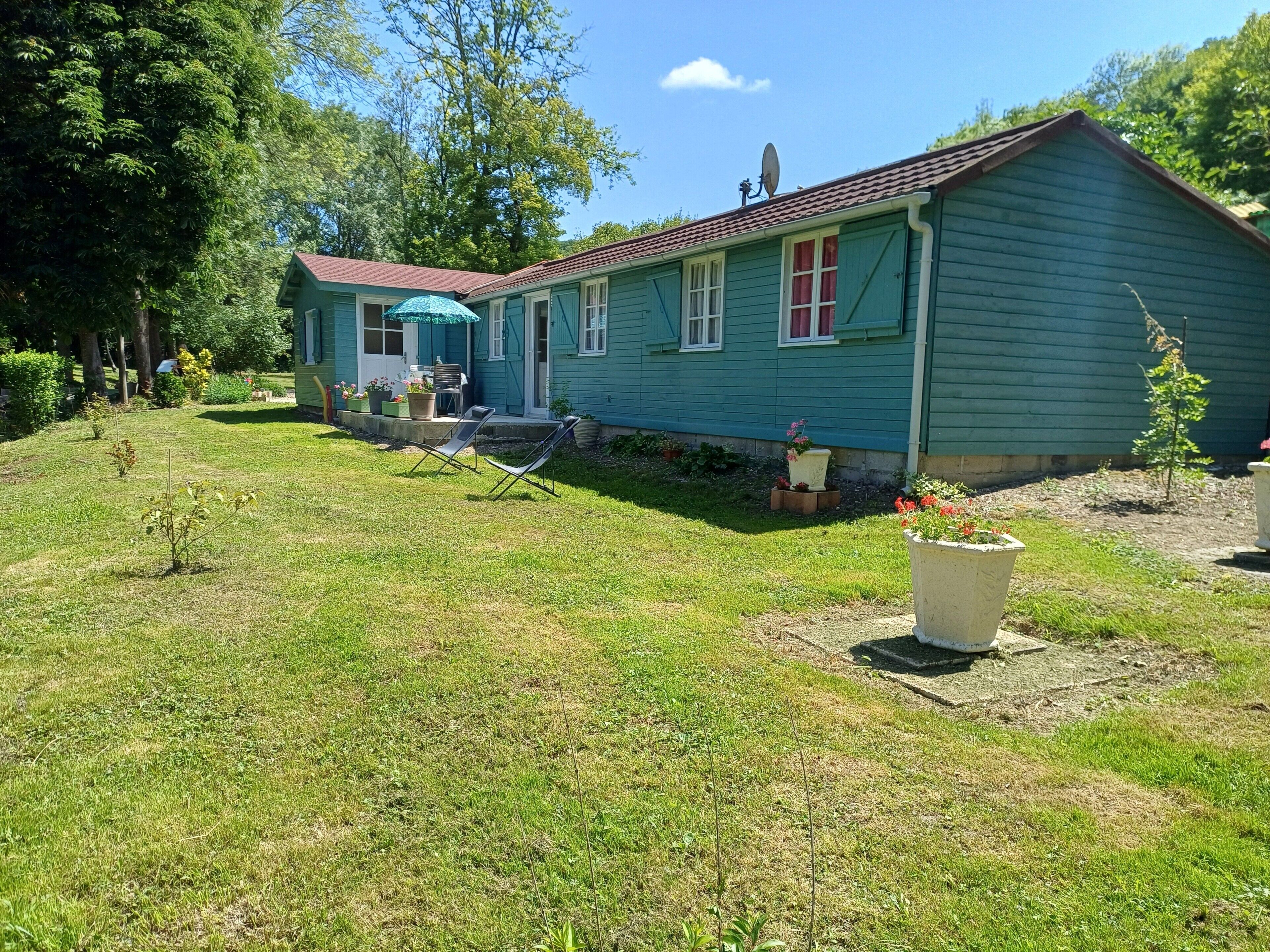 Una casa a due piani con facciata verde, un'antenna parabolica e un piccolo portico con una sedia.