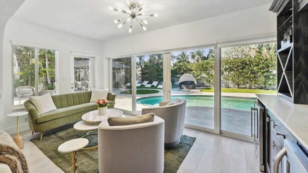 Un salon moderne avec un canapé vert, des fauteuils blancs et une vue sur la piscine.