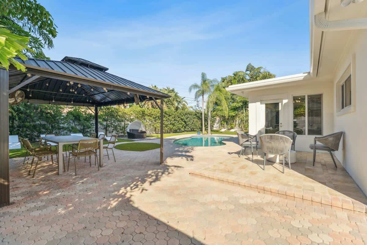 Un jardin avec une piscine, un espace salon extérieur et une terrasse couverte.