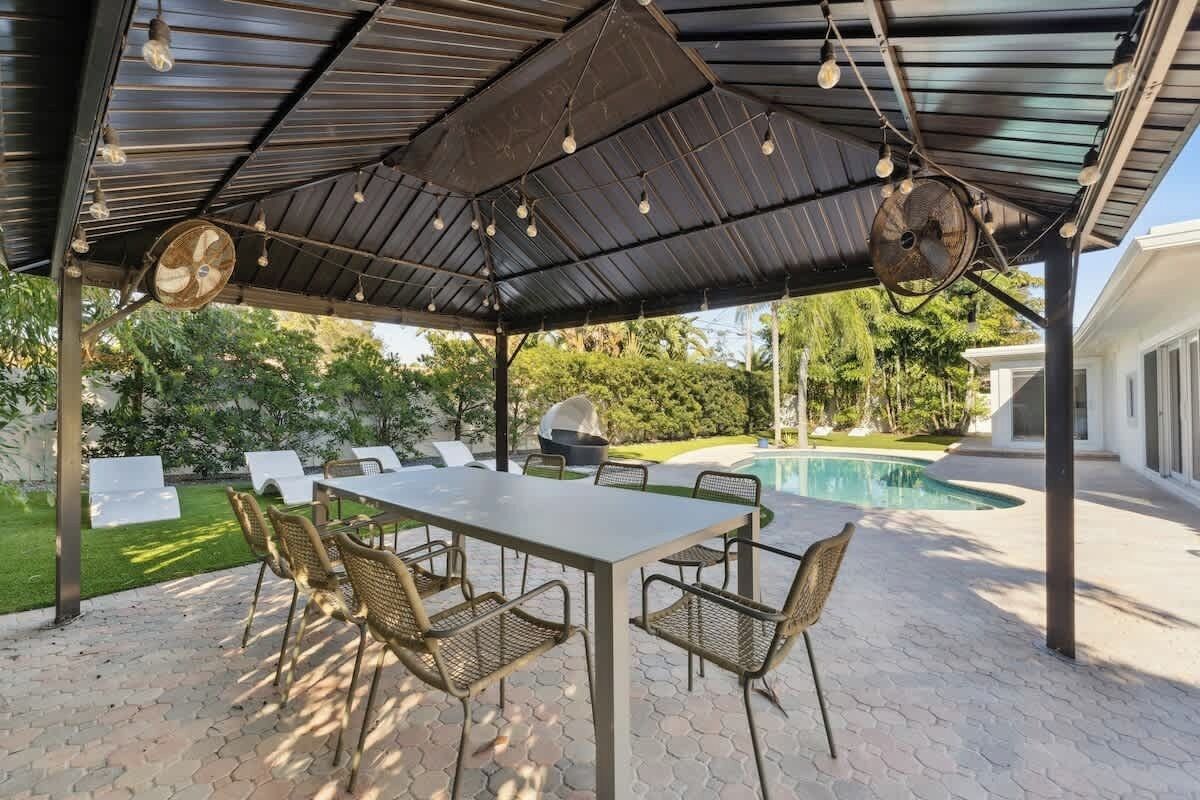 Une terrasse extérieure avec une table et des chaises, une piscine et un espace abrité équipé de ventilateurs.
