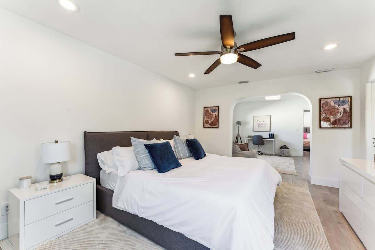 Un dormitorio moderno con una cama grande, un ventilador de techo y una mesita de noche con lámpara.