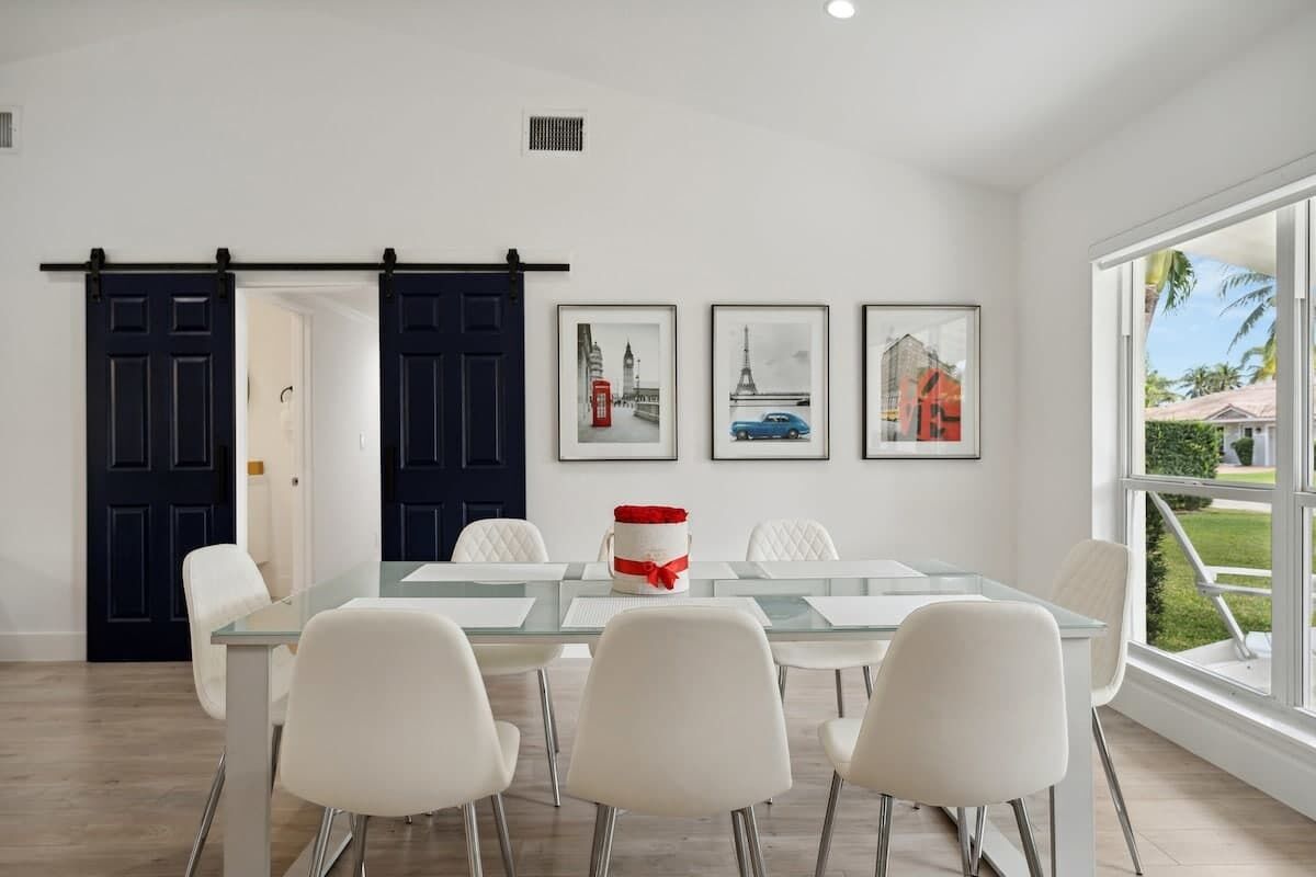 Un espace repas moderne avec une table en verre, des chaises blanches et des tableaux encadrés accrochés au mur.
