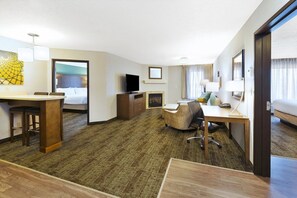 A hotel room with a bed, a desk, a TV, a fireplace, and a large window. - 2BR Executive Suite w/ Kitchen & Lounge (Columbia)