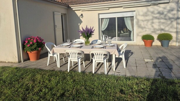 An outdoor patio with a table set for four, surrounded by white chairs, potted plants, and a window with curtains. - Large family home - 4 bedrooms, enclosed garden & terrace (Sainte-Radegonde)