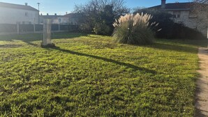 A grassy courtyard with a stone pillar, a bush, and a pathway leading to a building. - Large family home - 4 bedrooms, enclosed garden & terrace (Sainte-Radegonde)
