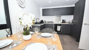 A modern kitchen with dark cabinets, a stainless steel range hood, and a dining area with a wooden table set for four. - Spacious 2 Bed Apartment in Central Liverpool (Liverpool)