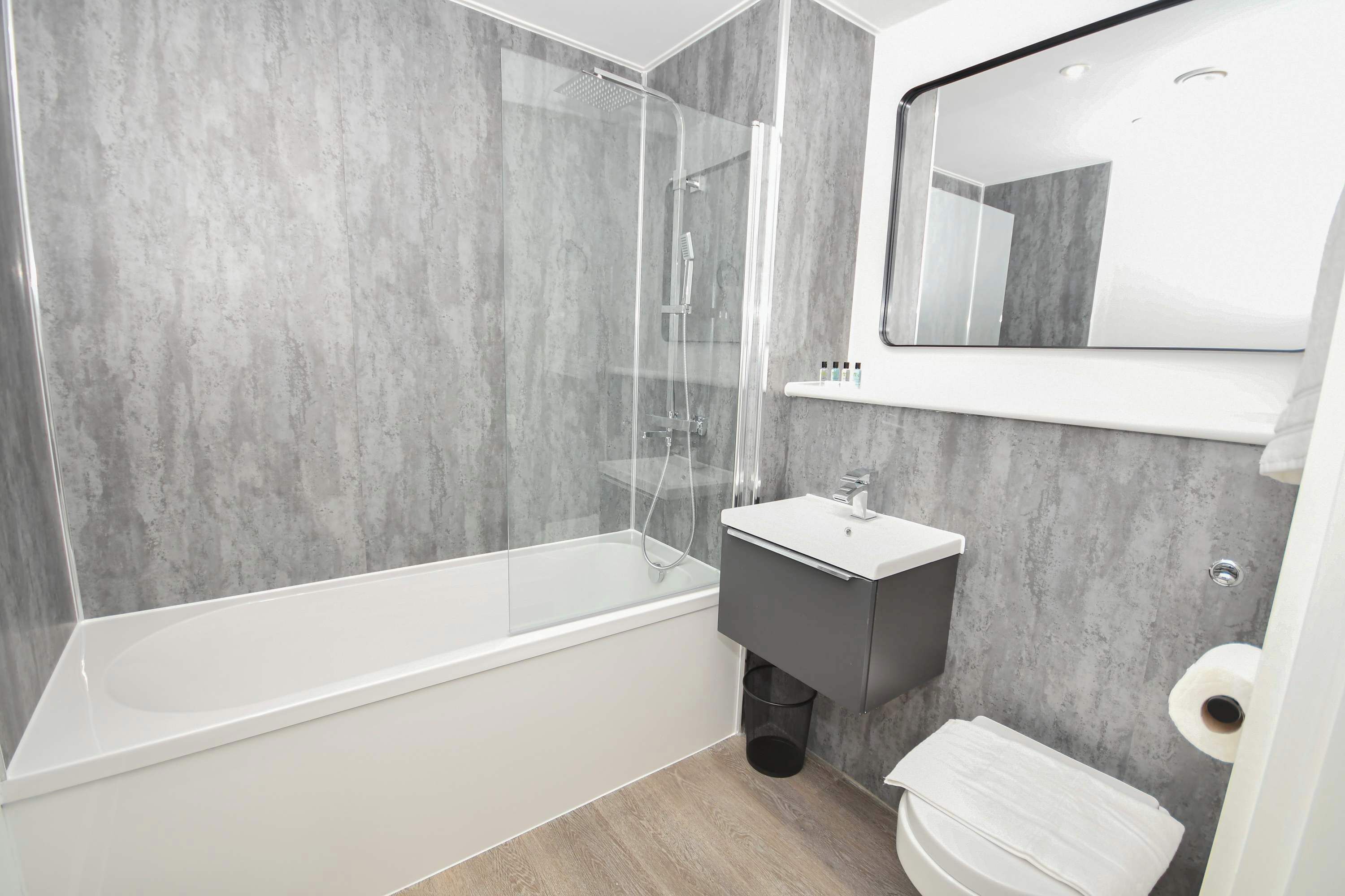Une salle de bain moderne avec une douche à parois de verre, une baignoire blanche, un lavabo gris et des toilettes.