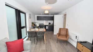 A modern living room with a grey sofa, a red pillow, a dining area with a table set for two, and a kitchen in the background. - Spacious 2 Bed Apartment in Central Liverpool (Liverpool)