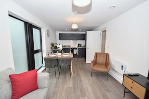 A modern living room with a grey sofa, a red pillow, a dining area with a table set for two, and a kitchen in the background. - Spacious 2 Bed Apartment in Central Liverpool (Liverpool)