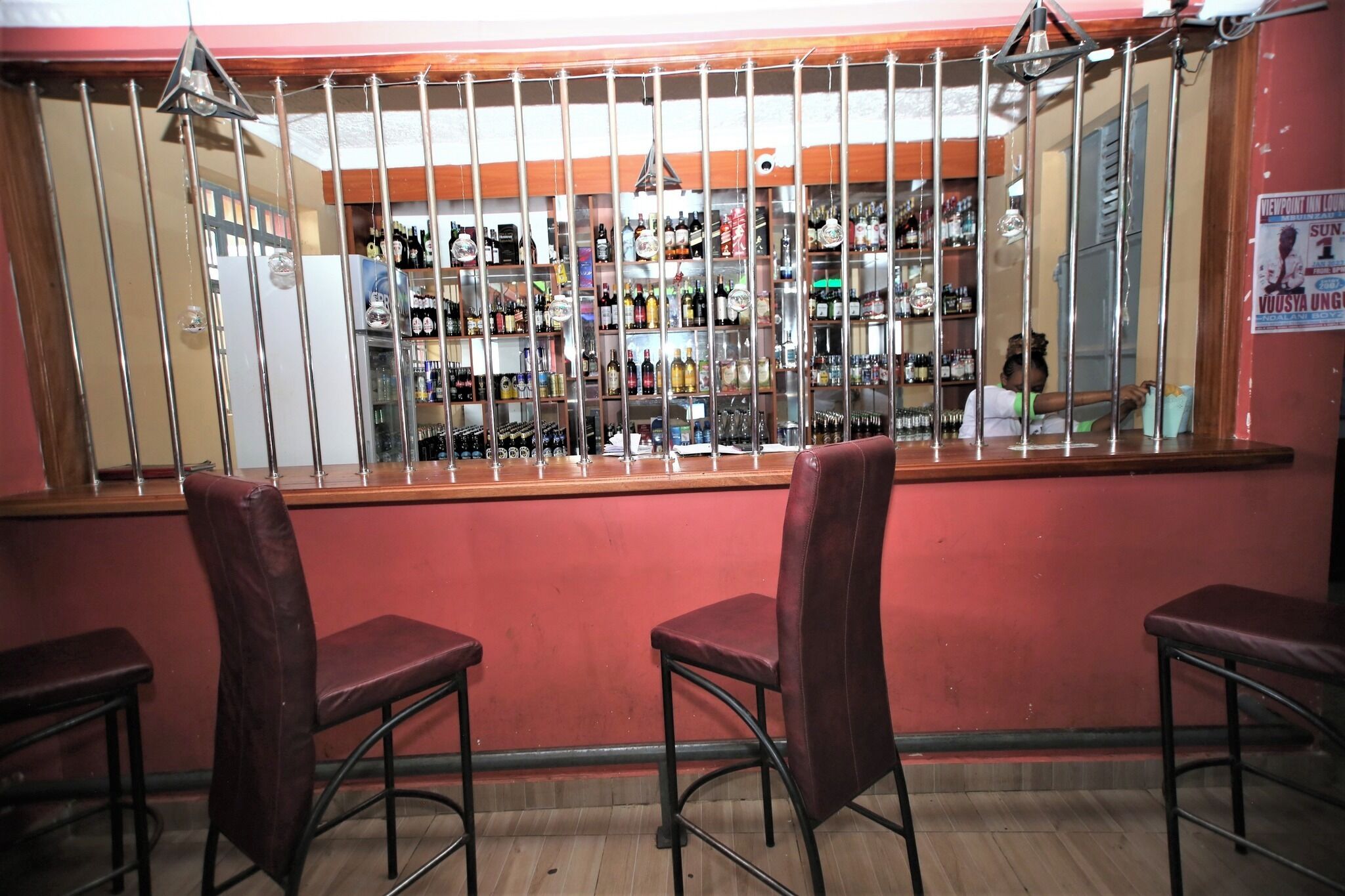 A bar area with a counter, shelves of bottles, and three bar stools.