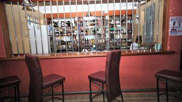 A bar area with a counter, shelves of bottles, and three bar stools.