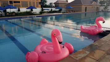 Piscina com boias de flamingo infláveis, área de estar externa e um edifício com fachada amarela.