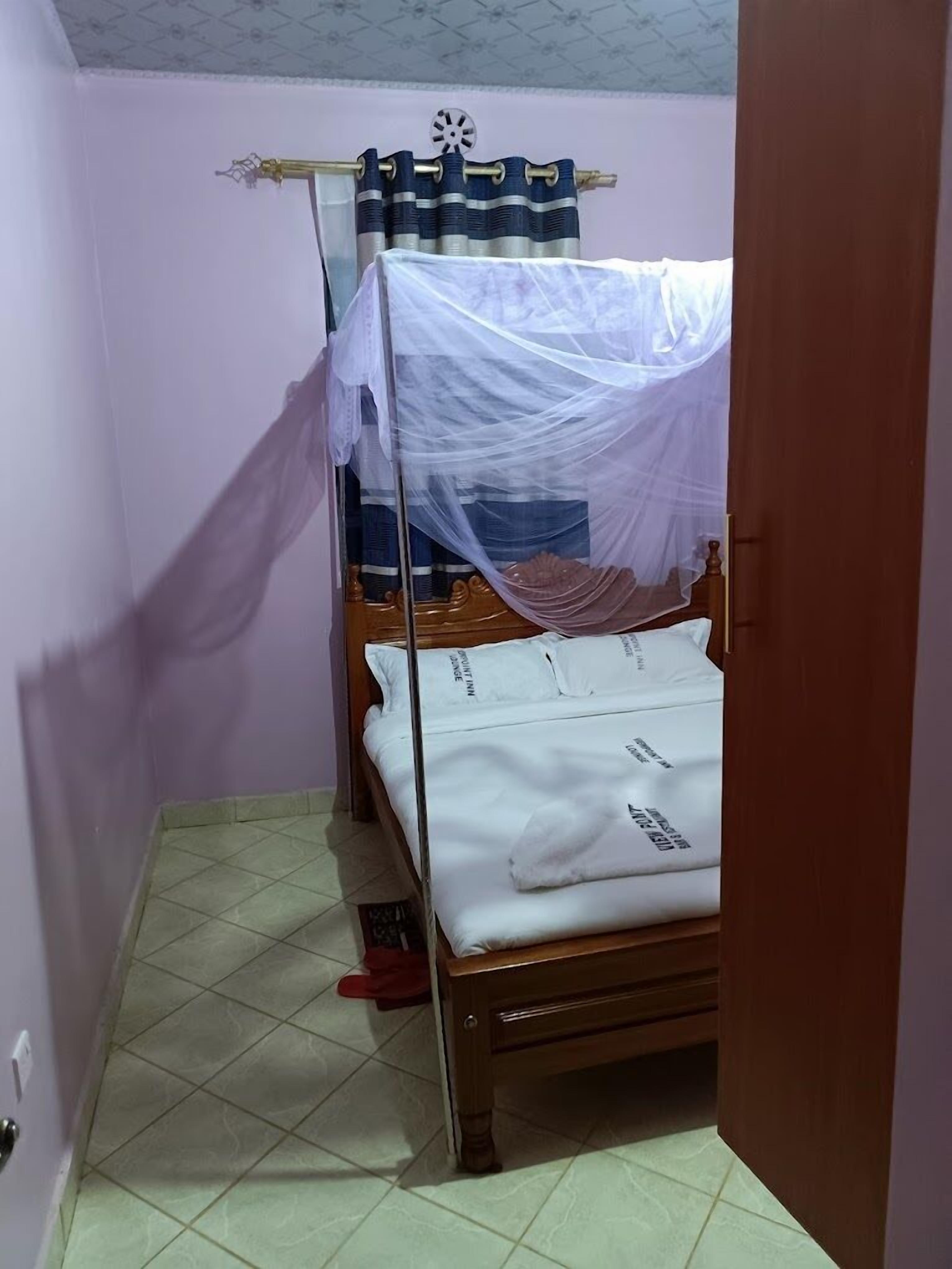 A small, narrow room with a single bed, a mosquito net, and a curtain.