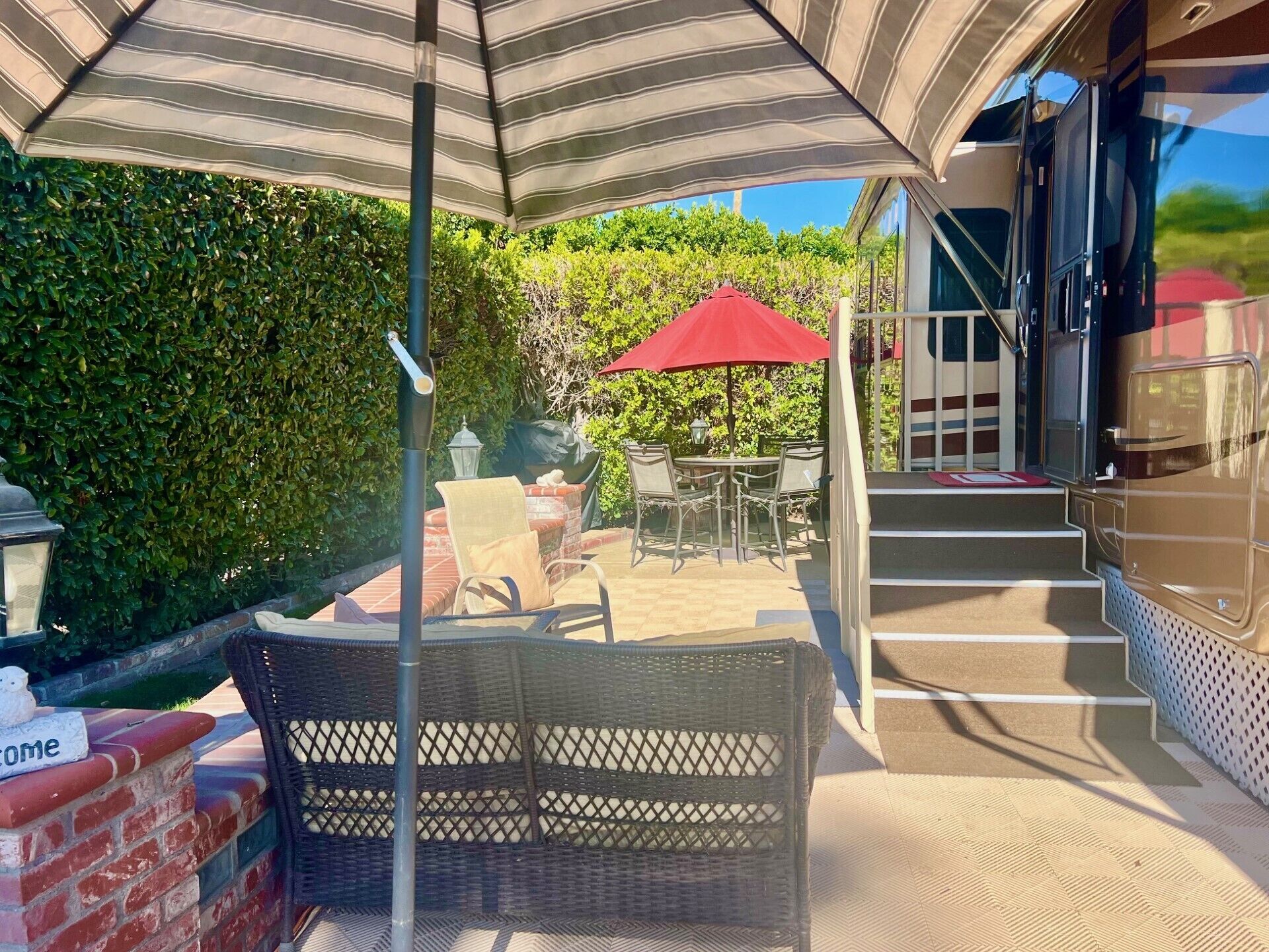 An outdoor patio area with wicker furniture, a red umbrella, and a brick wall.