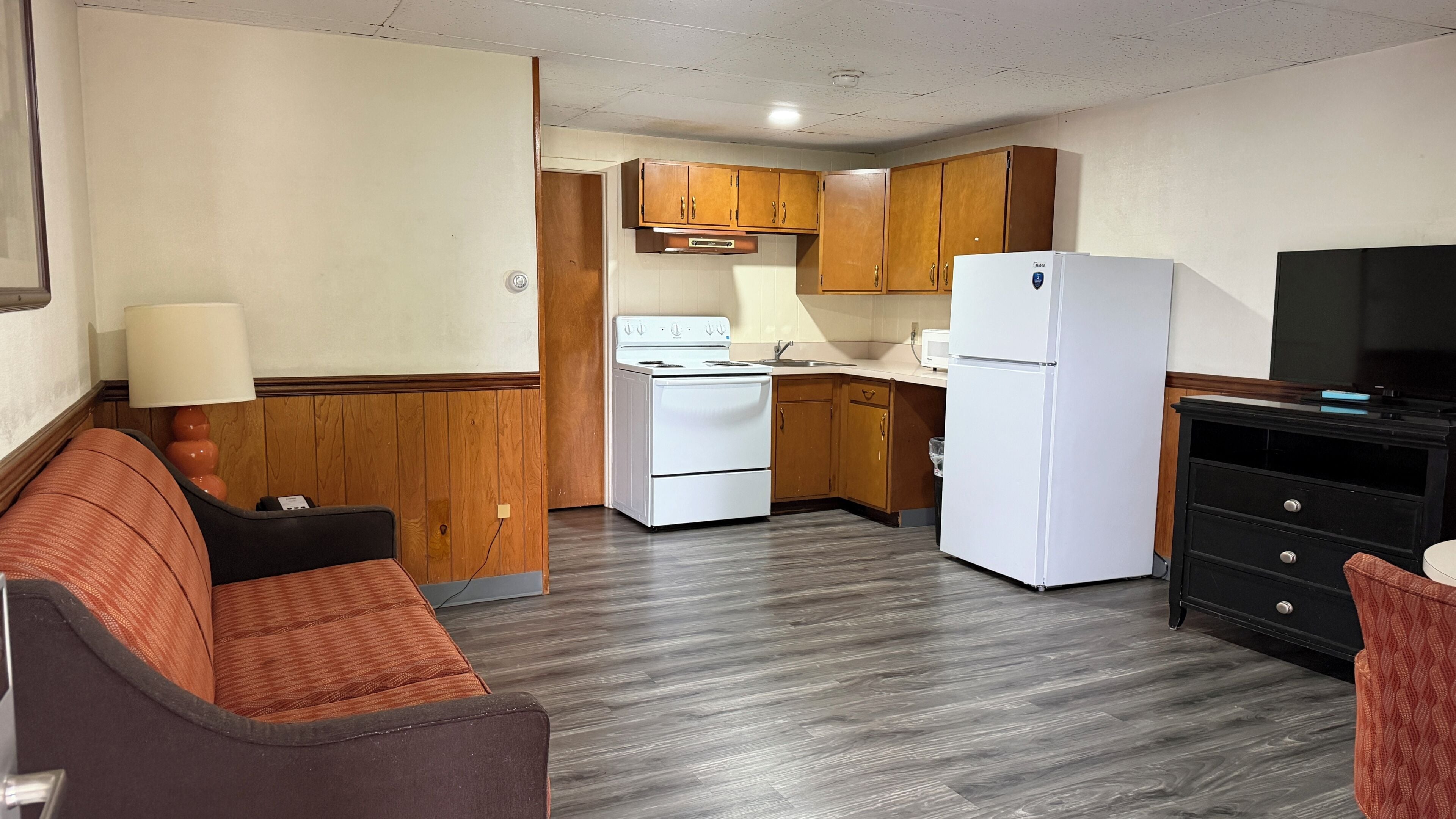 A compact kitchen with a stove, refrigerator, and wooden cabinets.