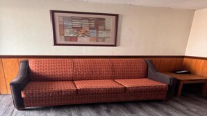 A red patterned sofa in a room with wooden paneling and a framed artwork on the wall.