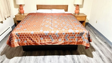 Uma cama com colcha estampada, duas mesas de cabeceira com abajures e um painel de madeira na cabeceira.