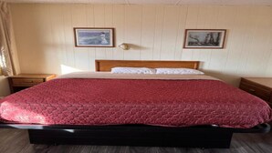 A hotel room with a large bed, wooden headboard, two bedside tables, and two framed pictures on the wall.